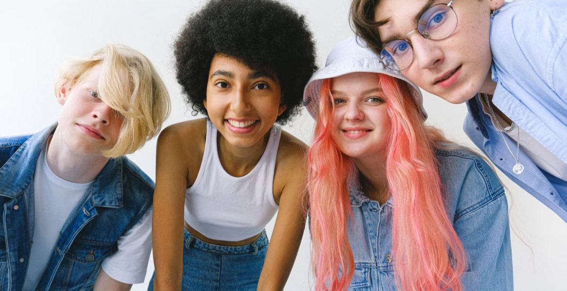 Low angle of group of cheerful multiethnic teenager friends standing together against white background and looking at camera