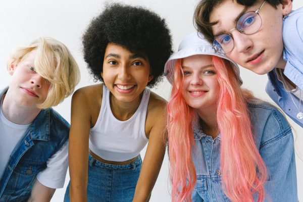Low angle of group of cheerful multiethnic teenager friends standing together against white background and looking at camera